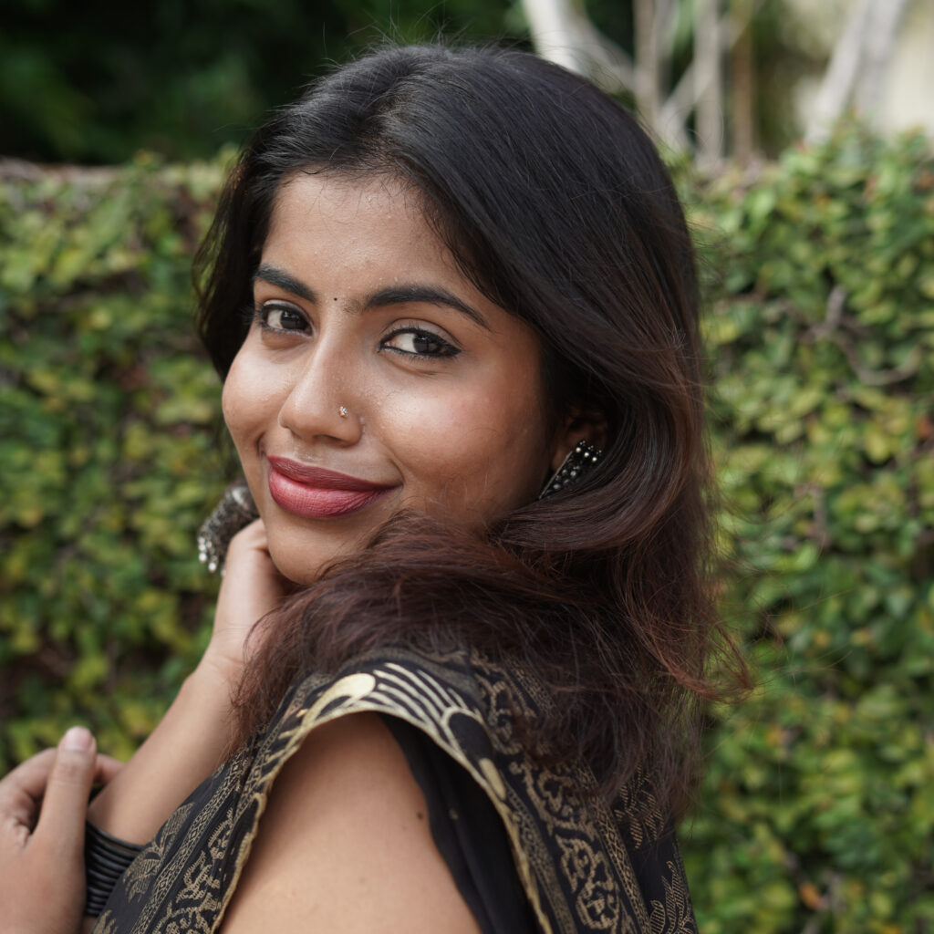 Smiling woman in a black and gold saree against a green wall