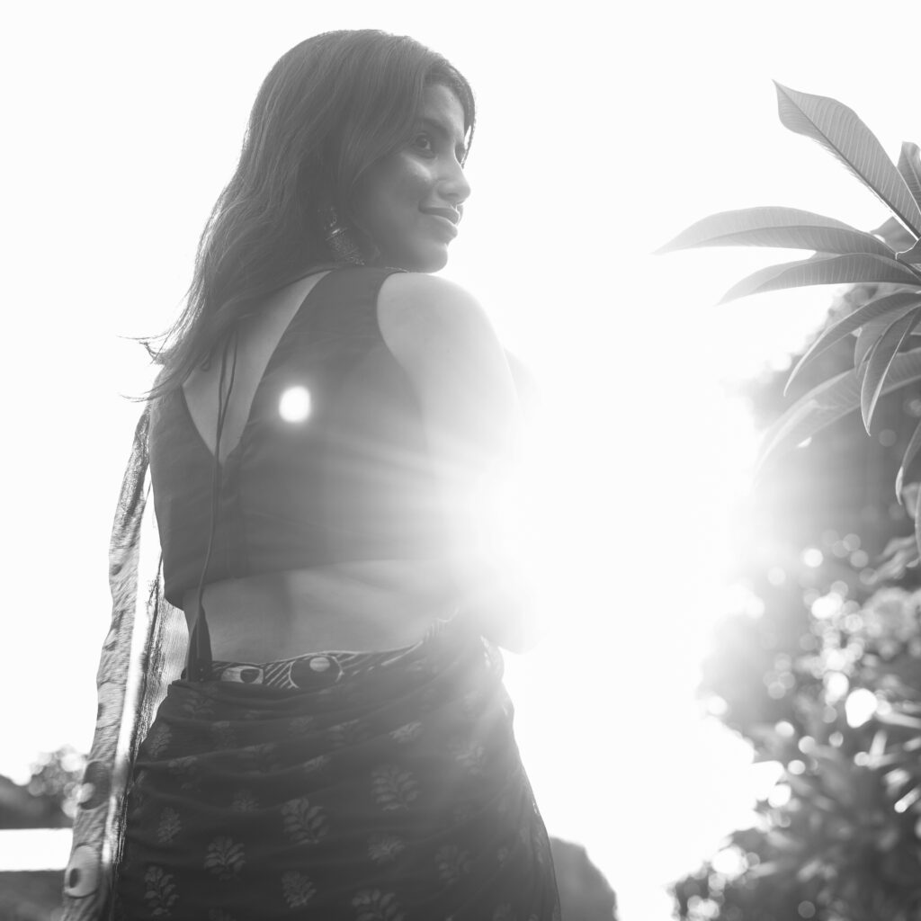 Black and white portrait of a woman in a saree with a bright sun flare behind her