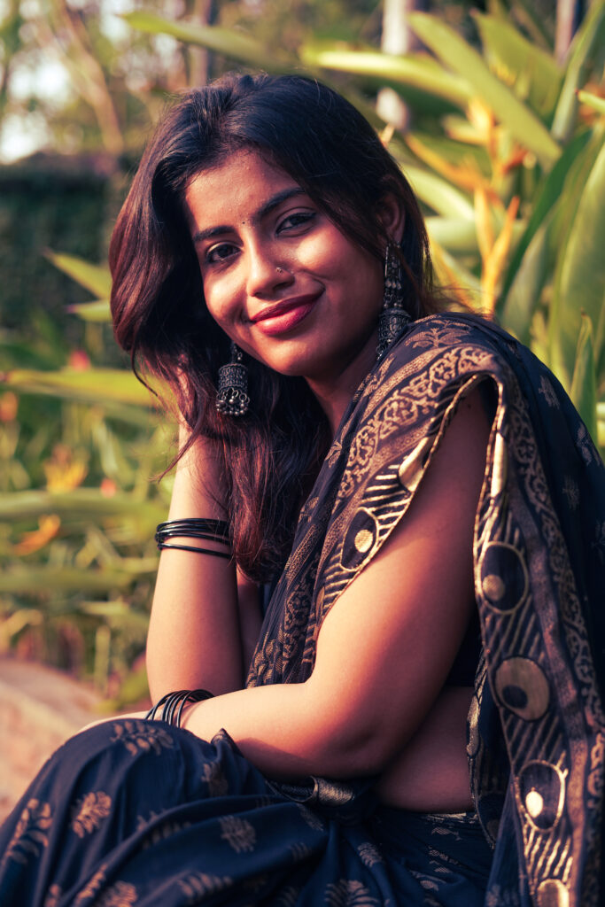 Close portrait of a smiling woman in a black and gold saree with silver jewellery, soft evening light