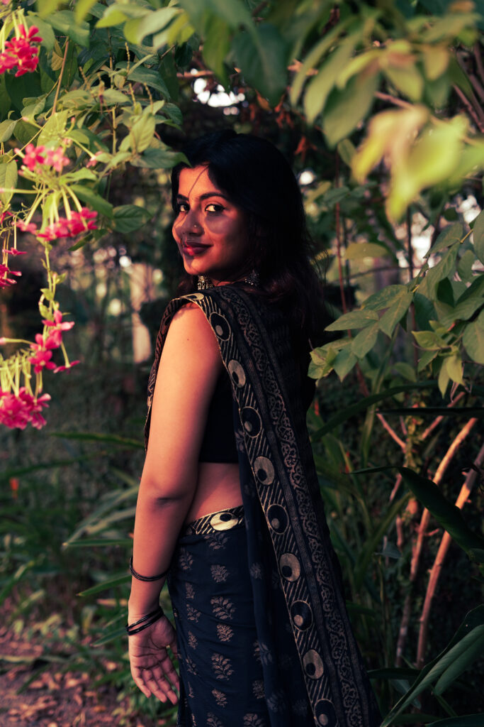 Woman in a black printed saree among pink flowers and leaves