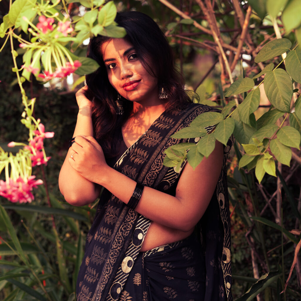 Woman in a black printed saree among pink flowers and leaves