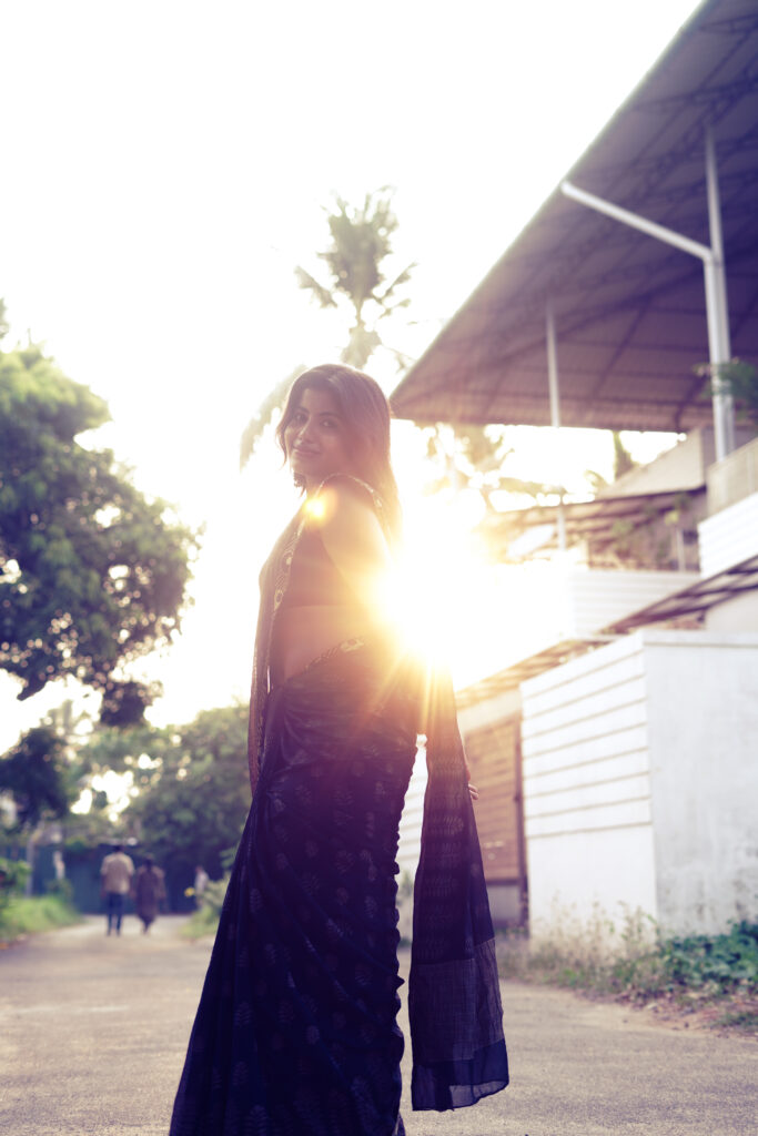 Woman in a black saree backlit by golden-hour sun on a quiet street
