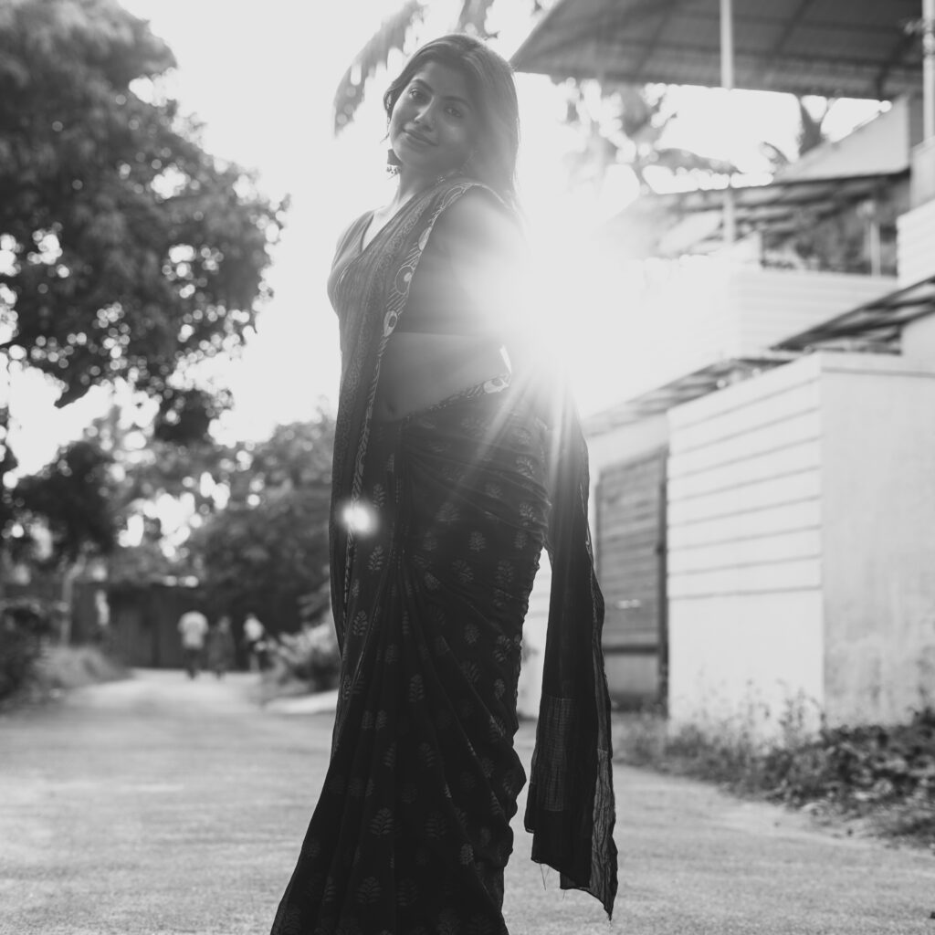 Black and white portrait of a woman in a saree with sun flare on a village road