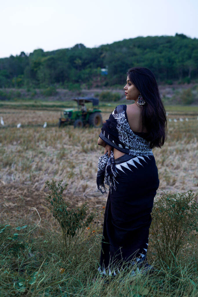 Woman in a black printed saree standing in a field at dusk