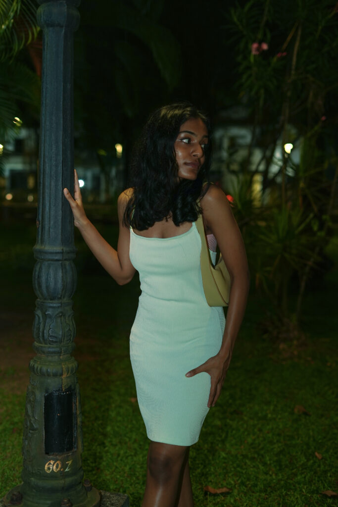 Woman in a mint dress beside an old iron lamp post at night