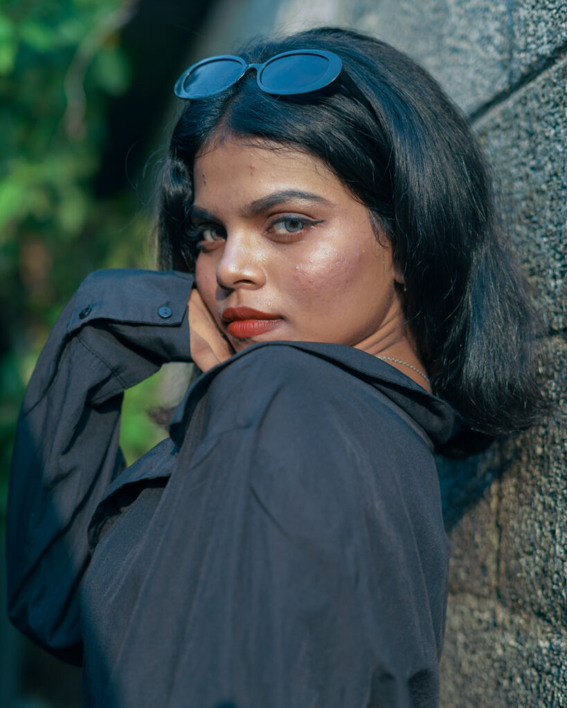 Woman in a black cropped shirt and skirt posing against a stone wall
