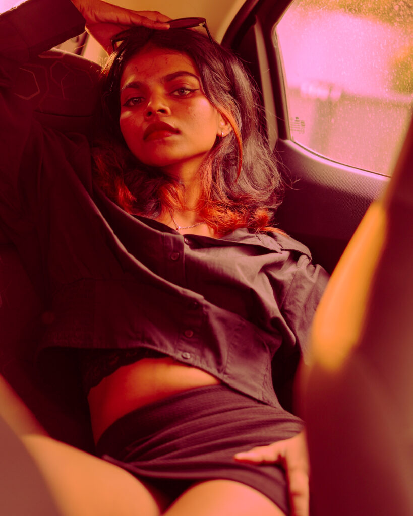 Moody editorial portrait of a woman reclining in a car lit with orange and pink light