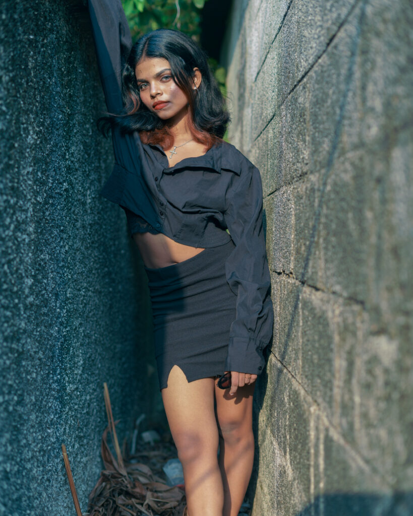 Woman in a black cropped shirt and skirt posing against a stone wall