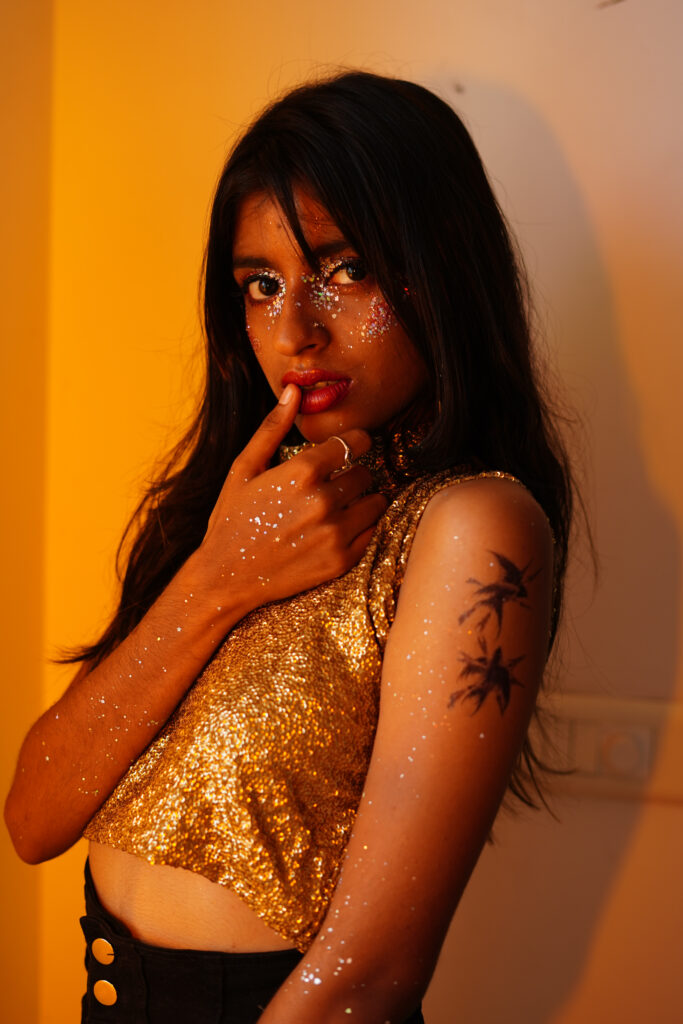 Editorial portrait of a woman with gold glitter on her face and body