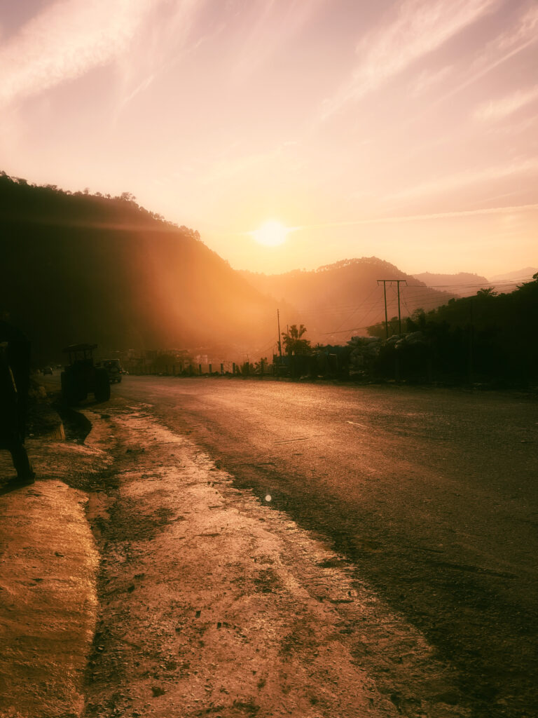 Sun setting over hills with a flare across a wet mountain road