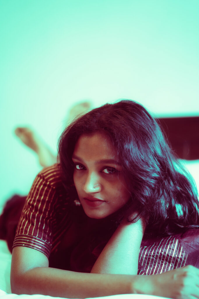 Woman lying on a bed resting her chin on her arms against a mint wall