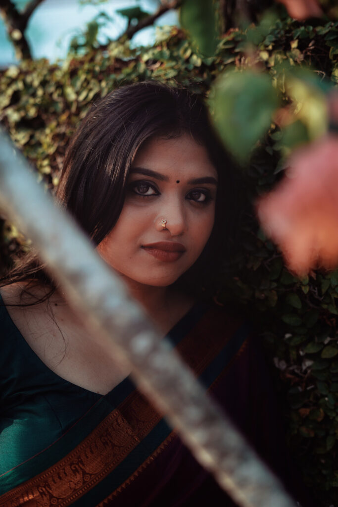 Woman in a magenta silk saree with a green blouse among plants and flowers