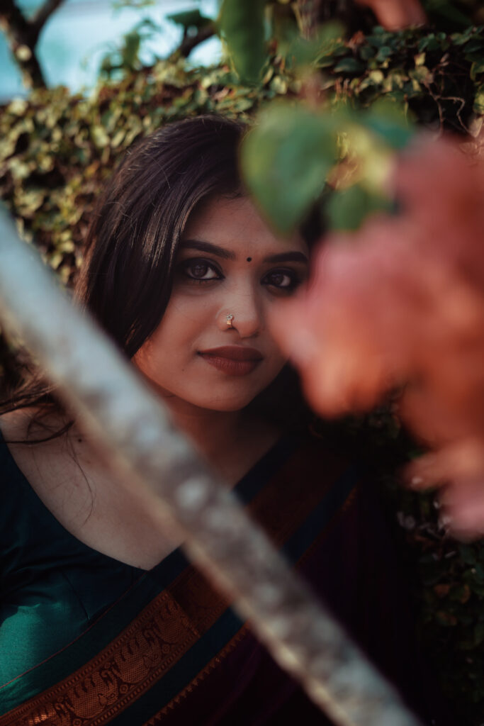 Woman in a magenta silk saree with a green blouse among plants and flowers