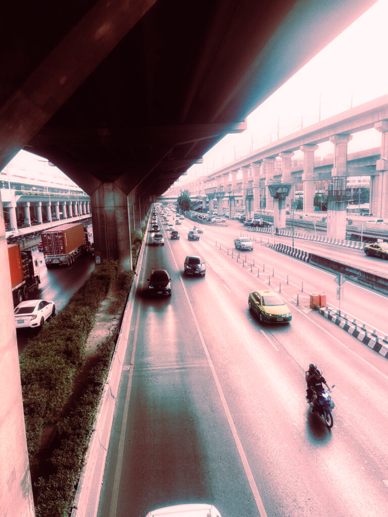 Traffic on a highway beneath a concrete metro flyover in soft pastel light