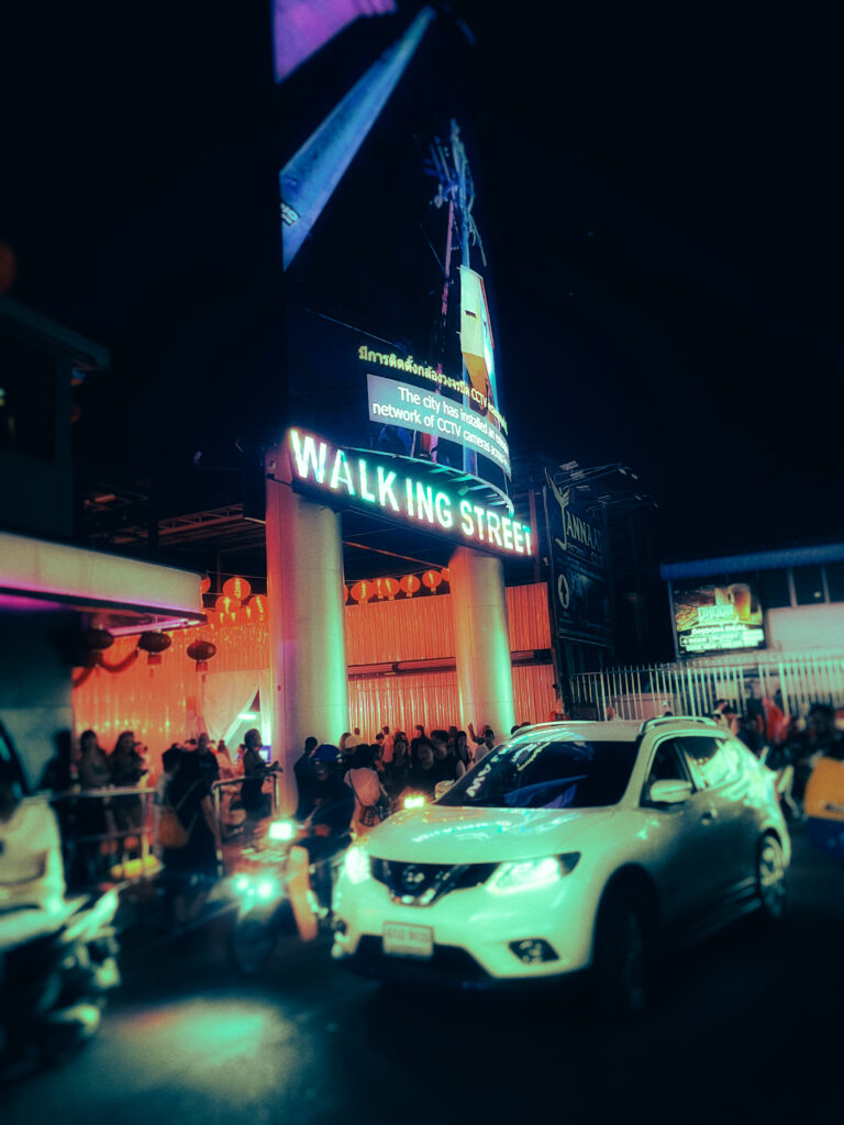 Neon-lit Walking Street at night with crowds and a white car