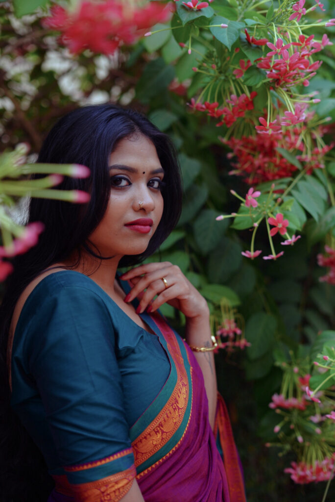 Woman in a magenta silk saree with a green blouse among plants and flowers
